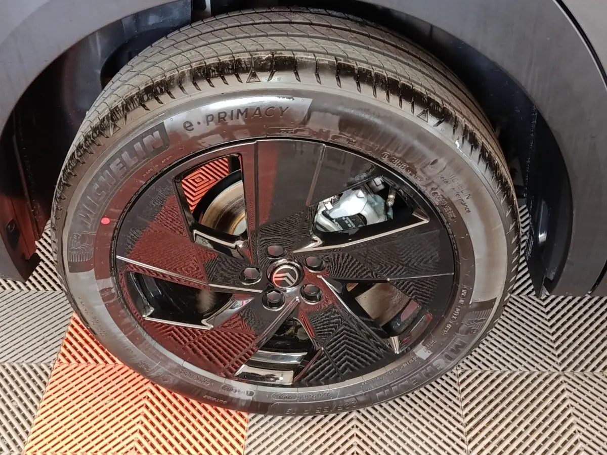 Gros plan sur la roue avant droite d'une Citroën C5 hybride gris foncé avec jante noire au design moderne.