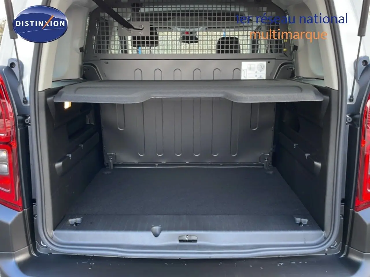 Coffre ouvert vu de l'arrière d'un Citroën Berlingo blanc glacier 2025 avec séparation grillagée et tablette de rangement.