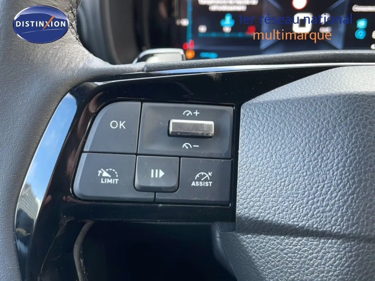 Gros plan sur les commandes au volant noir d’un Citroën Berlingo blanc glacier, avec affichage numérique en arrière-plan.