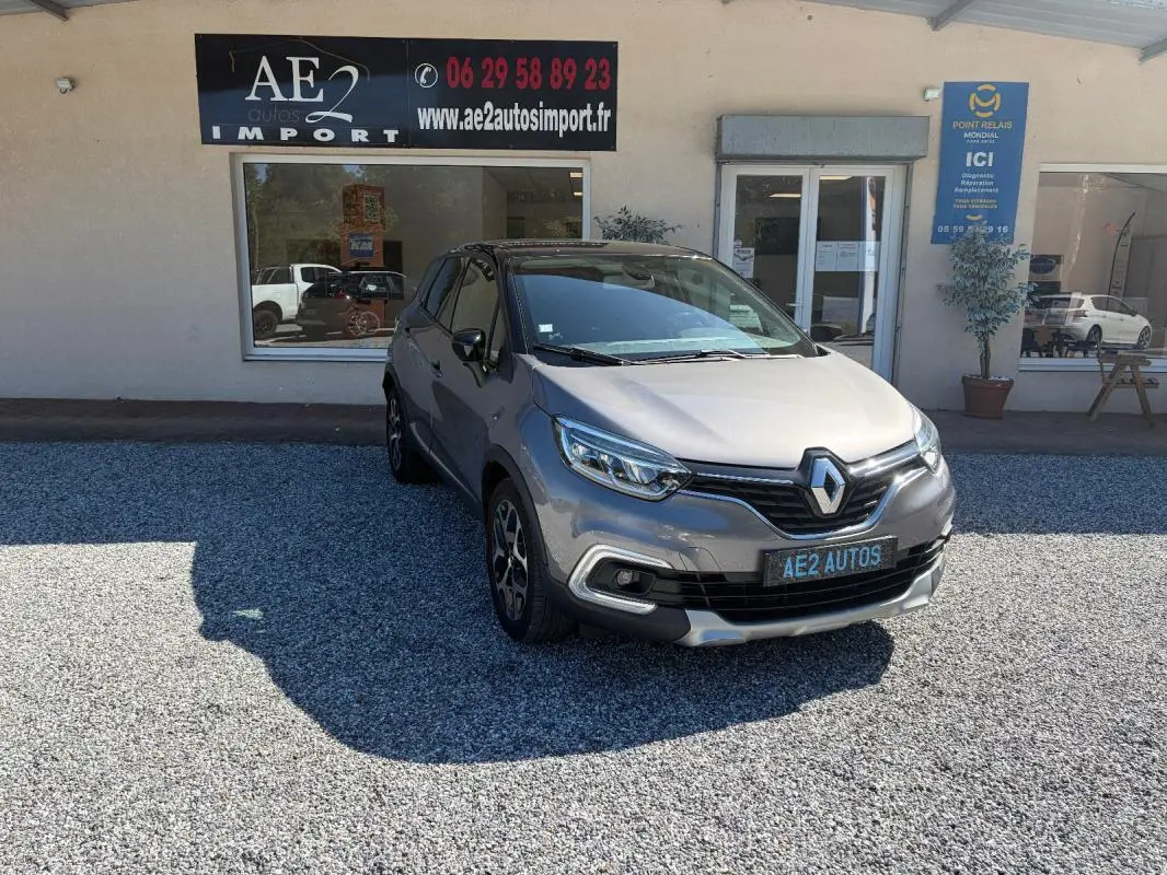 Renault Captur gris 3/4 avant droit, jantes alliage et calandre noire, stationné devant un garage AE2 Autos.