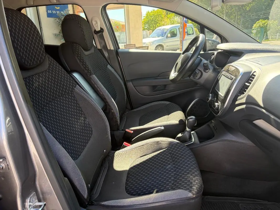 Vue intérieure côté conducteur du Renault Captur gris 2017, montrant sièges tissu, volant multifonctions et écran tactile central.