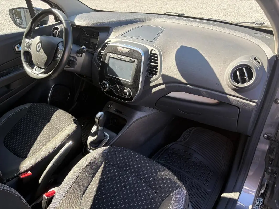 Vue intérieure côté conducteur du Renault Captur gris, montrant le volant multifonctions, la console centrale avec écran tactile et la boîte automatique.