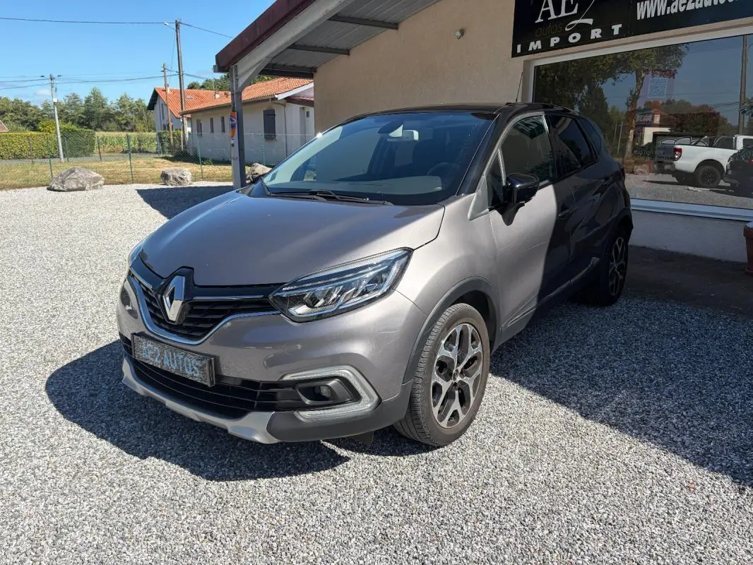Renault Captur gris 3/4 avant droit, avec jantes alliage et calandre noire brillante sous un soleil clair.
