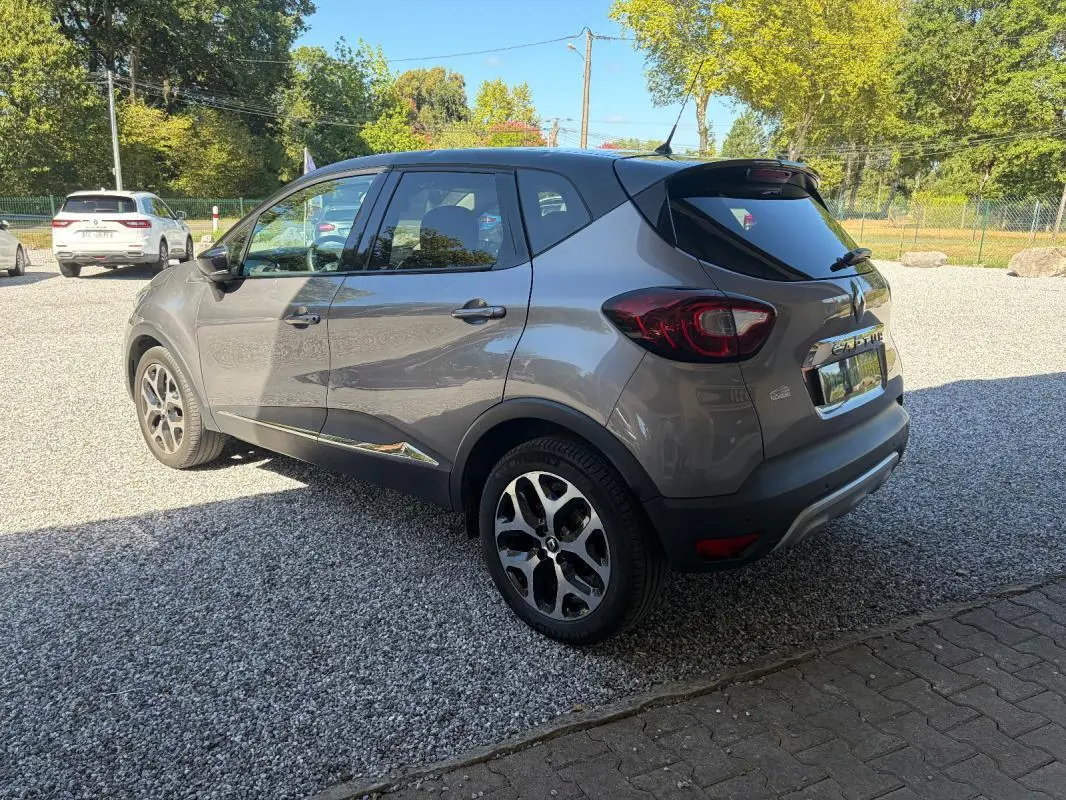 Renault Captur gris 3/4 arrière droit, jantes alliage et vitres teintées sous un ciel ensoleillé.