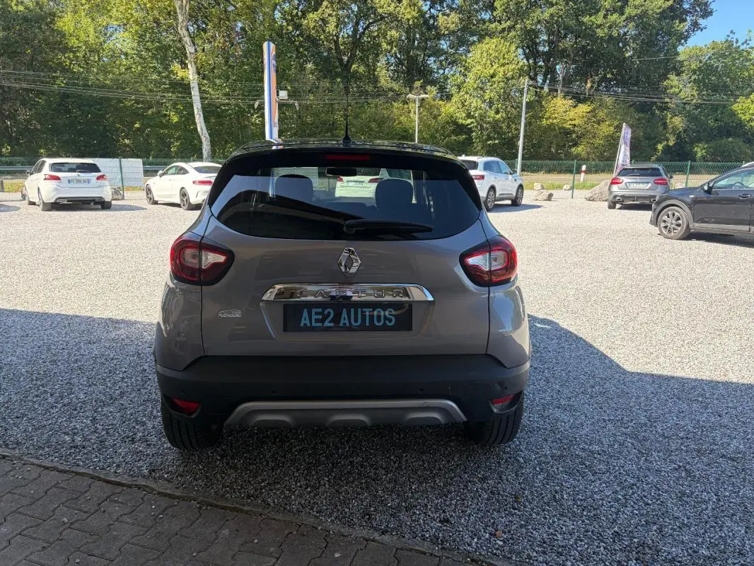 Vue arrière d'un Renault Captur gris 2017 avec jantes alliage et toit noir, stationné sur un sol gravillonné.