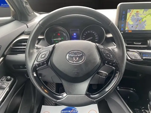 Vue centrée sur le volant noir du Toyota C-HR Hybride 2018, avec tableau de bord et écran GPS en arrière-plan.