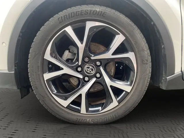 Gros plan sur la roue avant droite du Toyota C-HR Hybride blanc toit noir, jante alliage bicolore au design moderne.