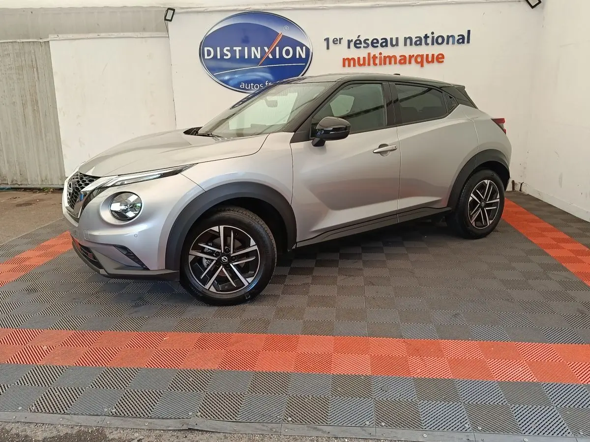 Vue de profil droit d'un Nissan Juke gris clair 2025 avec jantes alliage et toit noir dans un showroom.