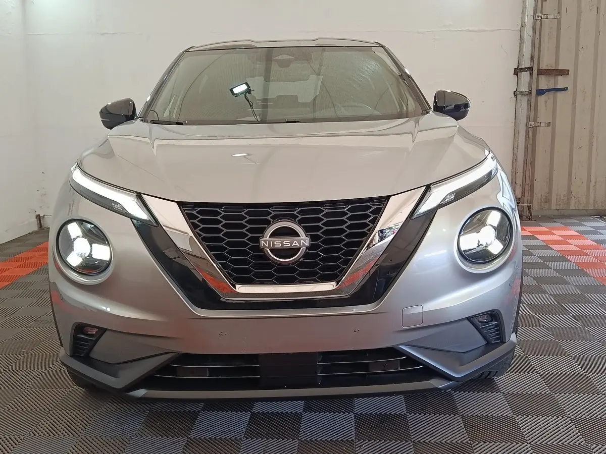 Vue frontale d'un Nissan Juke gris clair 2025 avec phares LED ronds et calandre en V chromée.