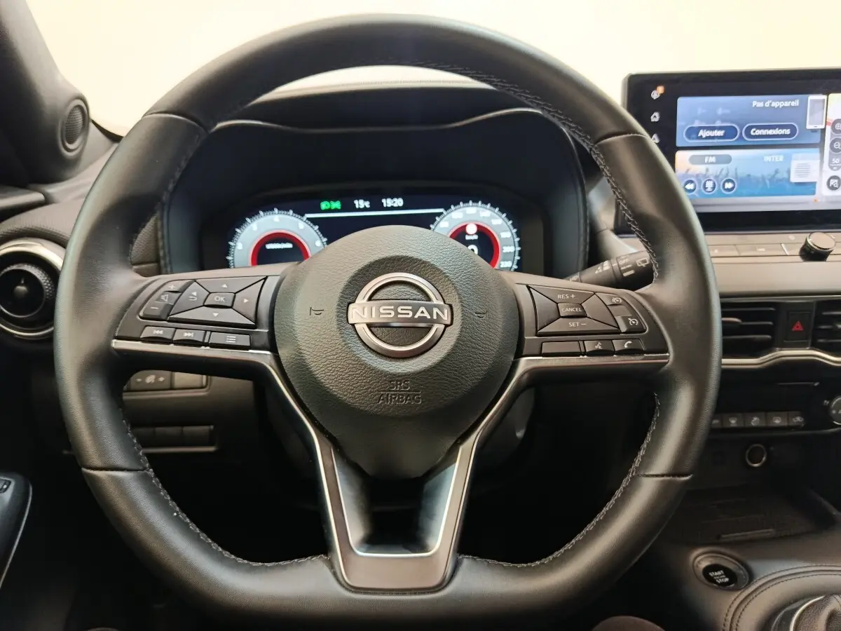 Vue rapprochée du volant noir multifonctions et du tableau de bord numérique du Nissan Juke 2025 essence gris clair.