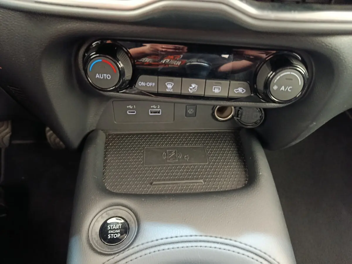 Vue rapprochée de la console centrale noire du Nissan Juke 2025 avec commandes climatisation et bouton start/stop.