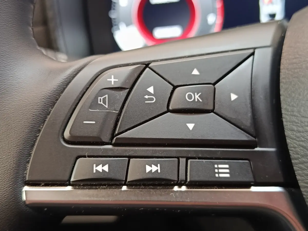 Gros plan sur les commandes multifonctions noires du volant du Nissan Juke 2025, avec affichage numérique flou en arrière-plan.