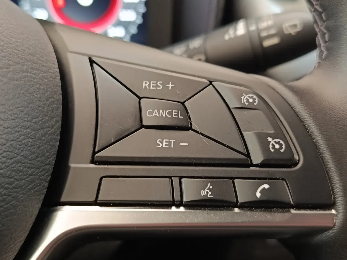 Gros plan sur les commandes du régulateur de vitesse et téléphone au volant du Nissan Juke gris clair 2025.