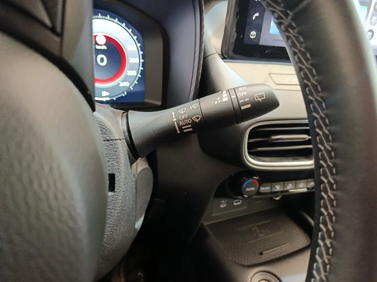Gros plan sur le commodo d’essuie-glace à gauche du volant du Nissan Juke gris clair, avec tableau de bord et écran tactile en arrière-plan.