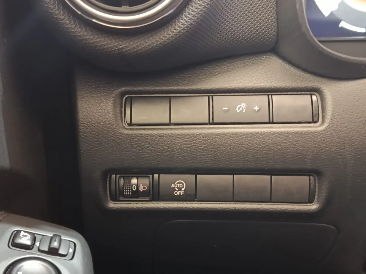 Gros plan sur les commandes de réglage des phares et luminosité du tableau de bord d'un Nissan Juke gris clair.