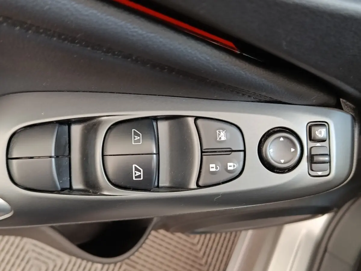 Gros plan sur les commandes de lève-vitres et rétroviseurs côté conducteur d’un Nissan Juke 2025 gris clair.