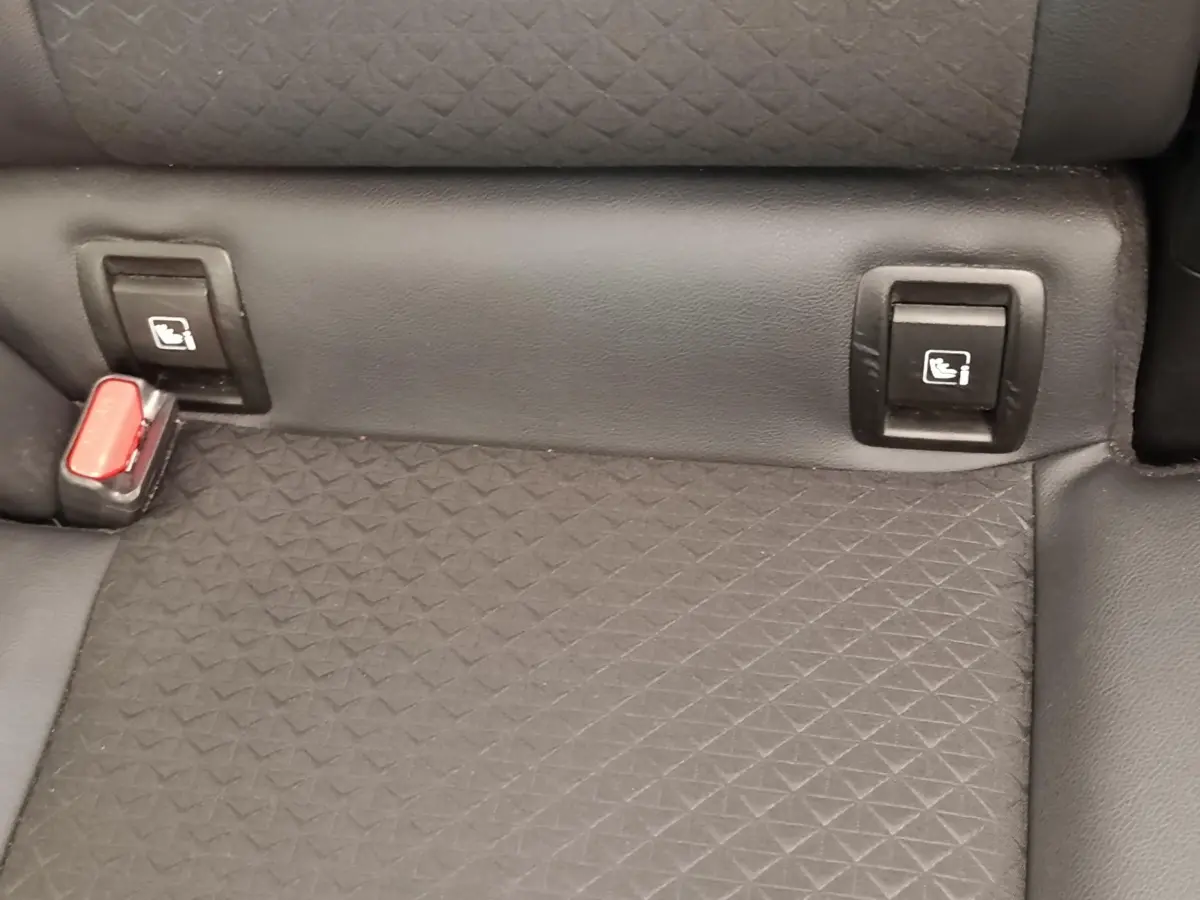 Gros plan sur la banquette arrière noire du Nissan Juke avec fixation Isofix et boucle de ceinture rouge visible.