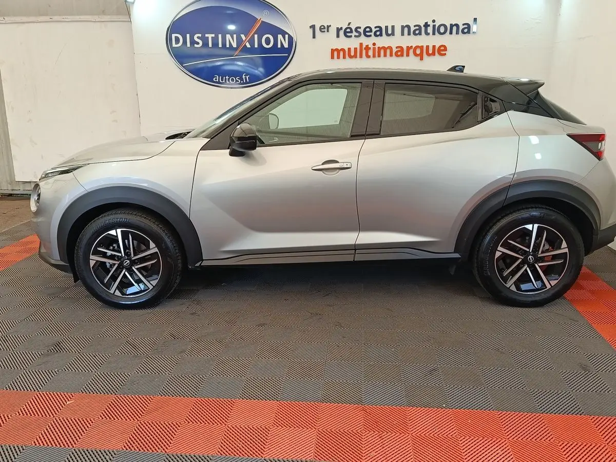 Vue de profil côté gauche d'un Nissan Juke gris clair 2025 avec toit noir et jantes alliage bicolores.