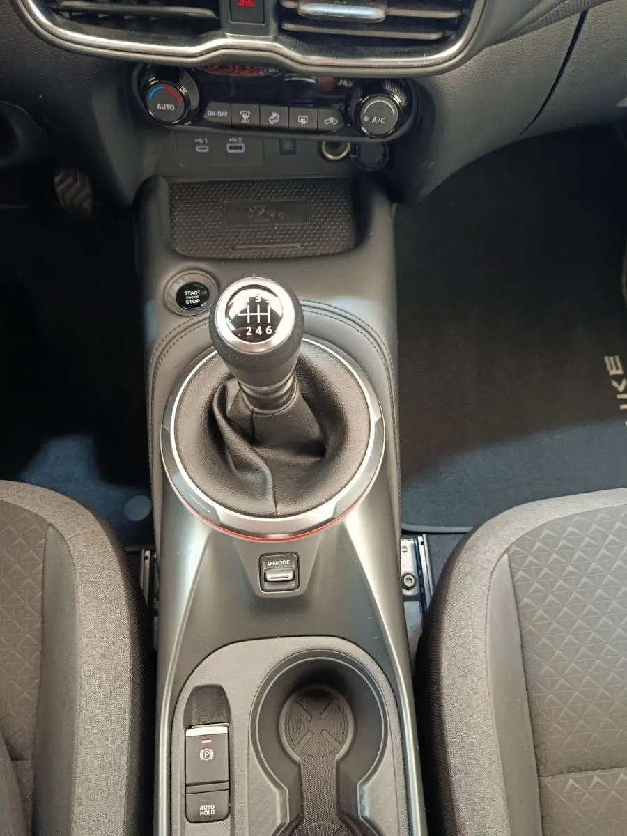 Vue intérieure centrée sur la console centrale du Nissan Juke gris clair, mettant en valeur le levier de vitesse manuel et les commandes.