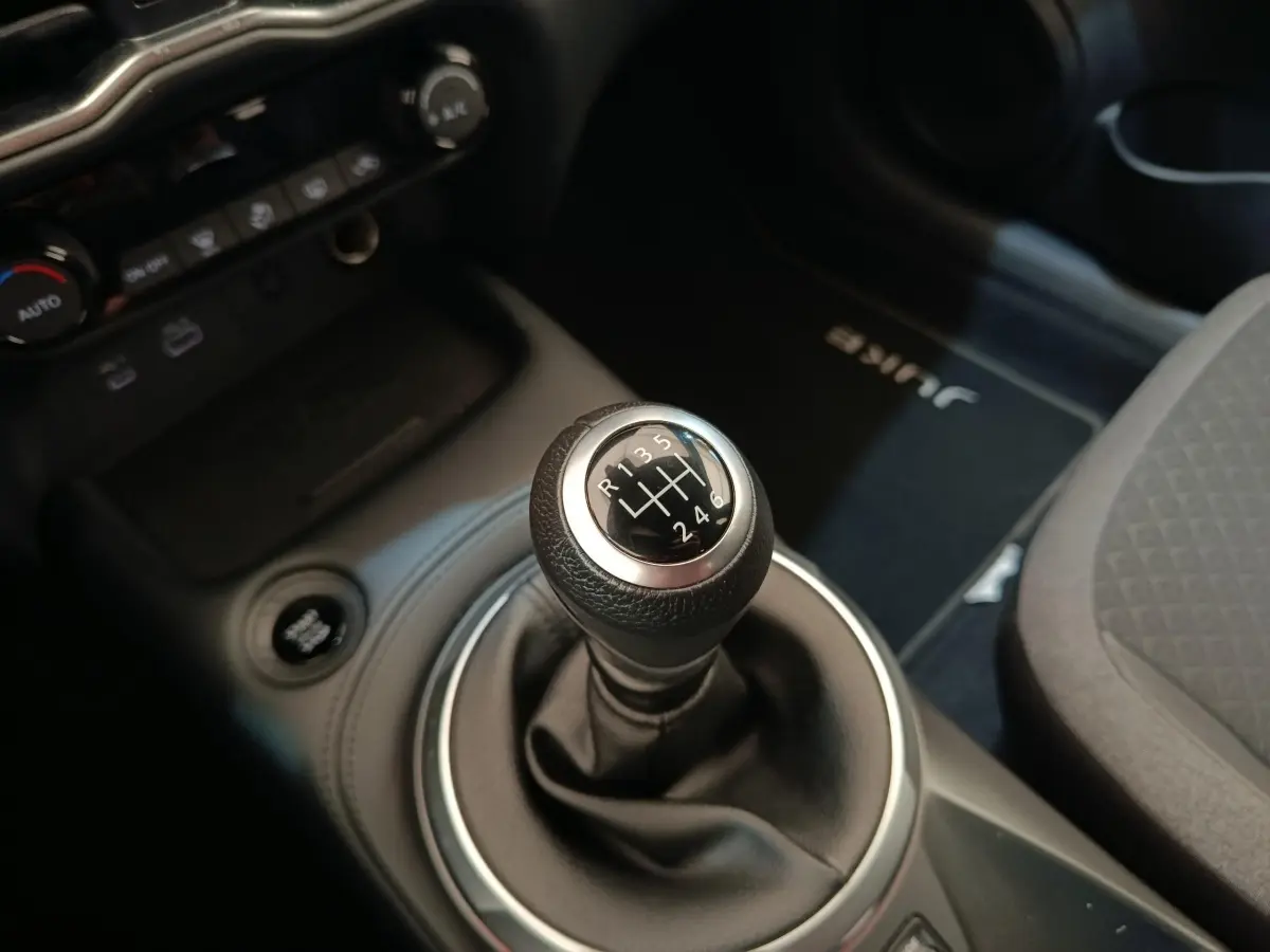 Gros plan sur le levier de vitesse manuel noir du Nissan Juke gris clair, avec tapis marqué "JUKE" visible côté passager.