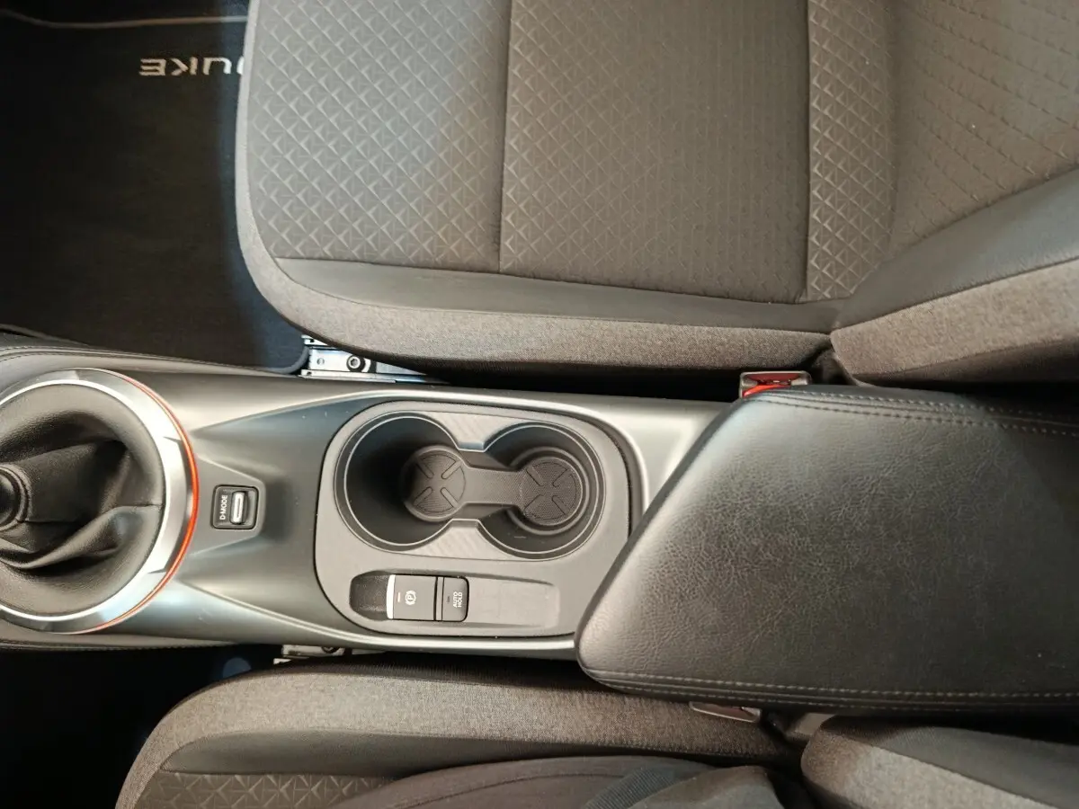 Vue plongeante sur la console centrale noire avec levier de vitesse et accoudoir en cuir du Nissan Juke gris clair 2025.