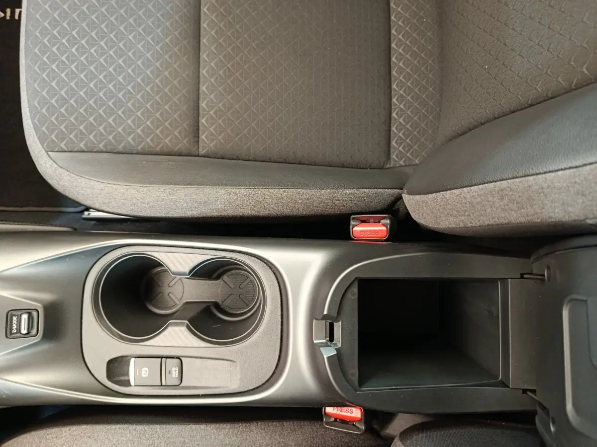 Vue plongeante sur la console centrale noire avec porte-gobelets et accoudoir ouvert du Nissan Juke gris clair.