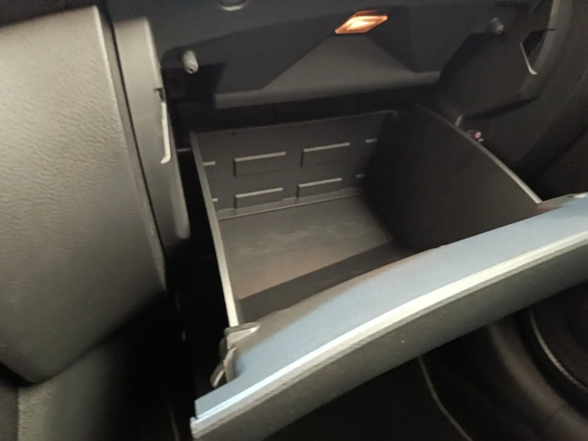 Gros plan sur la boîte à gants ouverte côté passager du Nissan Juke gris clair, montrant l'intérieur vide et la texture du tableau de bord.