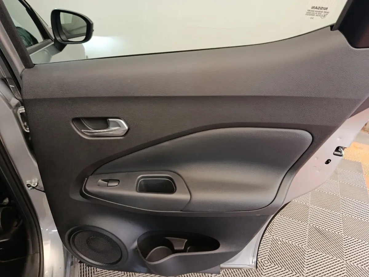 Vue intérieure de la porte avant gauche du Nissan Juke gris clair 2025, avec poignée et haut-parleur intégrés.