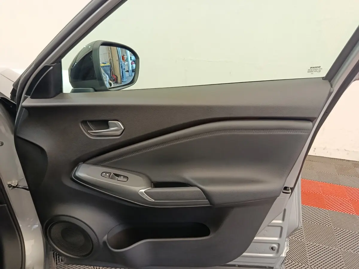 Vue intérieure de la porte avant gauche gris clair du Nissan Juke 2025 avec commandes de vitres et haut-parleur intégré.