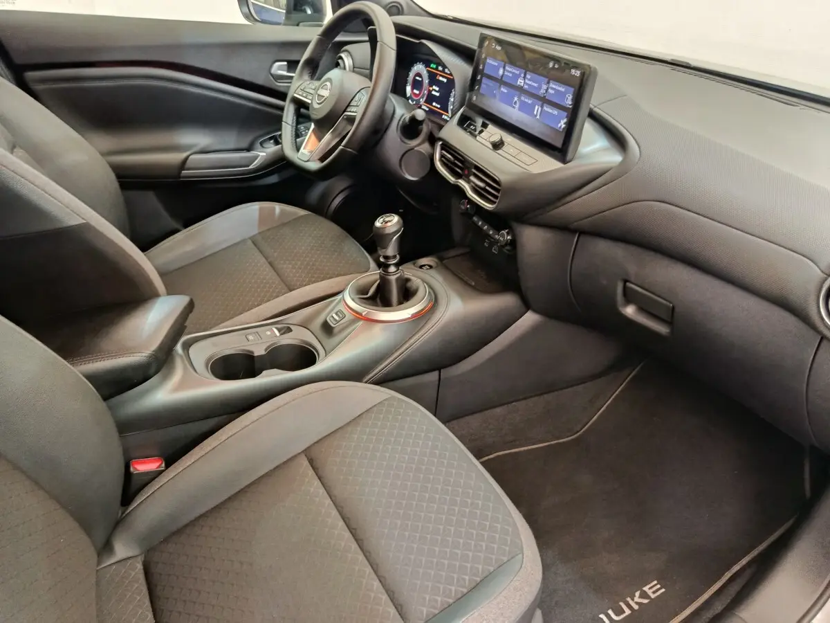 Intérieur avant droit du Nissan Juke gris clair 2025, volant multifonctions, écran tactile et boîte manuelle visible.