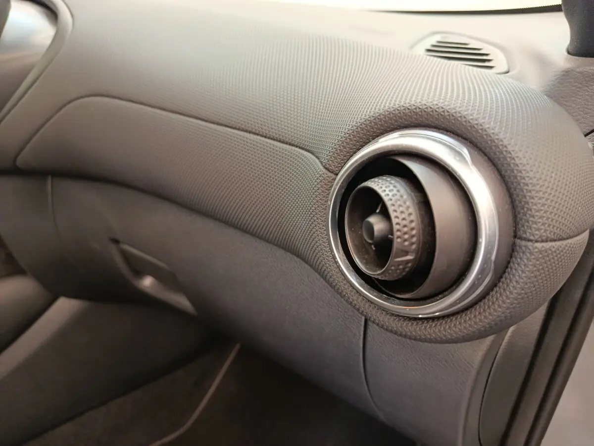 Détail de la sortie d'air ronde avec finition texturée du tableau de bord gris foncé du Nissan Juke 2025 côté passager.