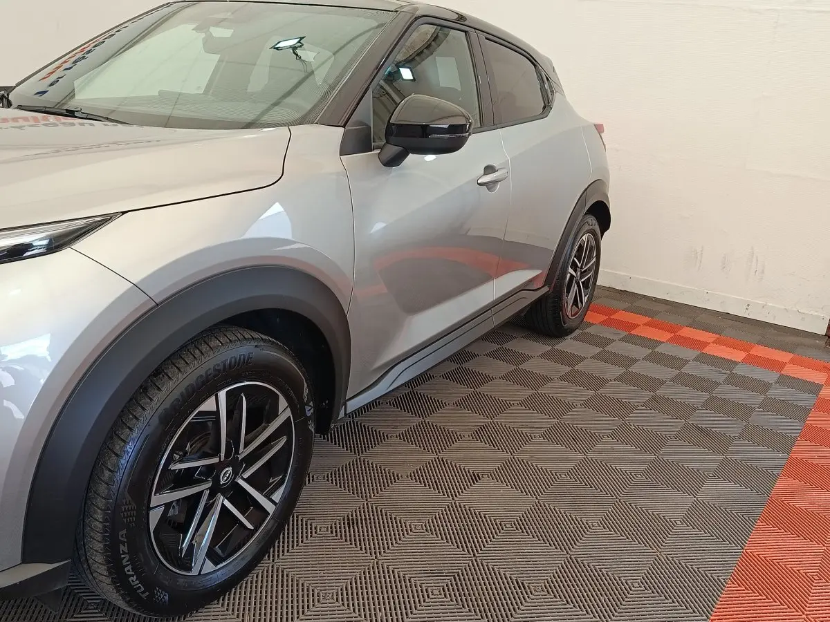 Vue 3/4 avant droit d'un Nissan Juke gris clair avec jantes noires et arches de roue noires contrastantes.