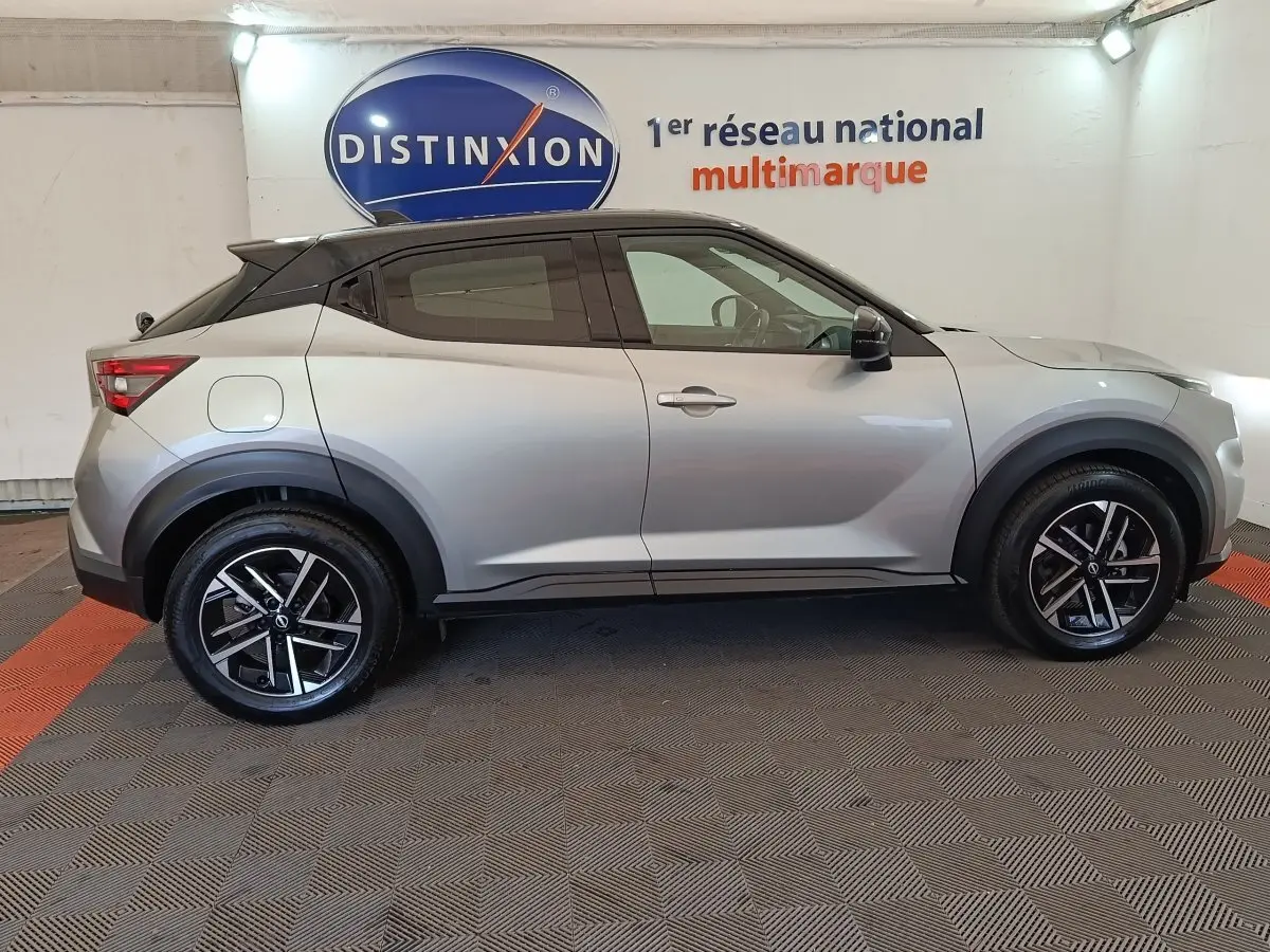 Profil droit d'un Nissan Juke 2025 gris clair avec toit noir, jantes alliage et protections d'ailes noires.