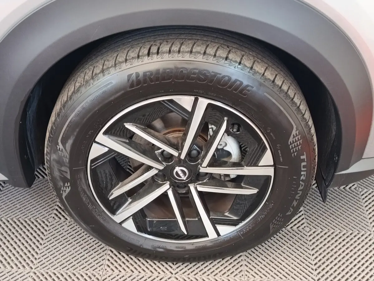 Gros plan sur la roue avant droite du Nissan Juke gris clair, avec jante alliage noire et argentée au design moderne.