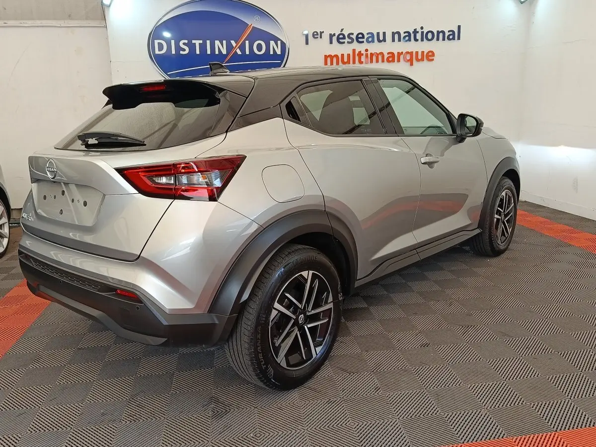 Nissan Juke gris clair vu en 3/4 arrière droit, avec jantes alliage noires et toit noir contrasté.