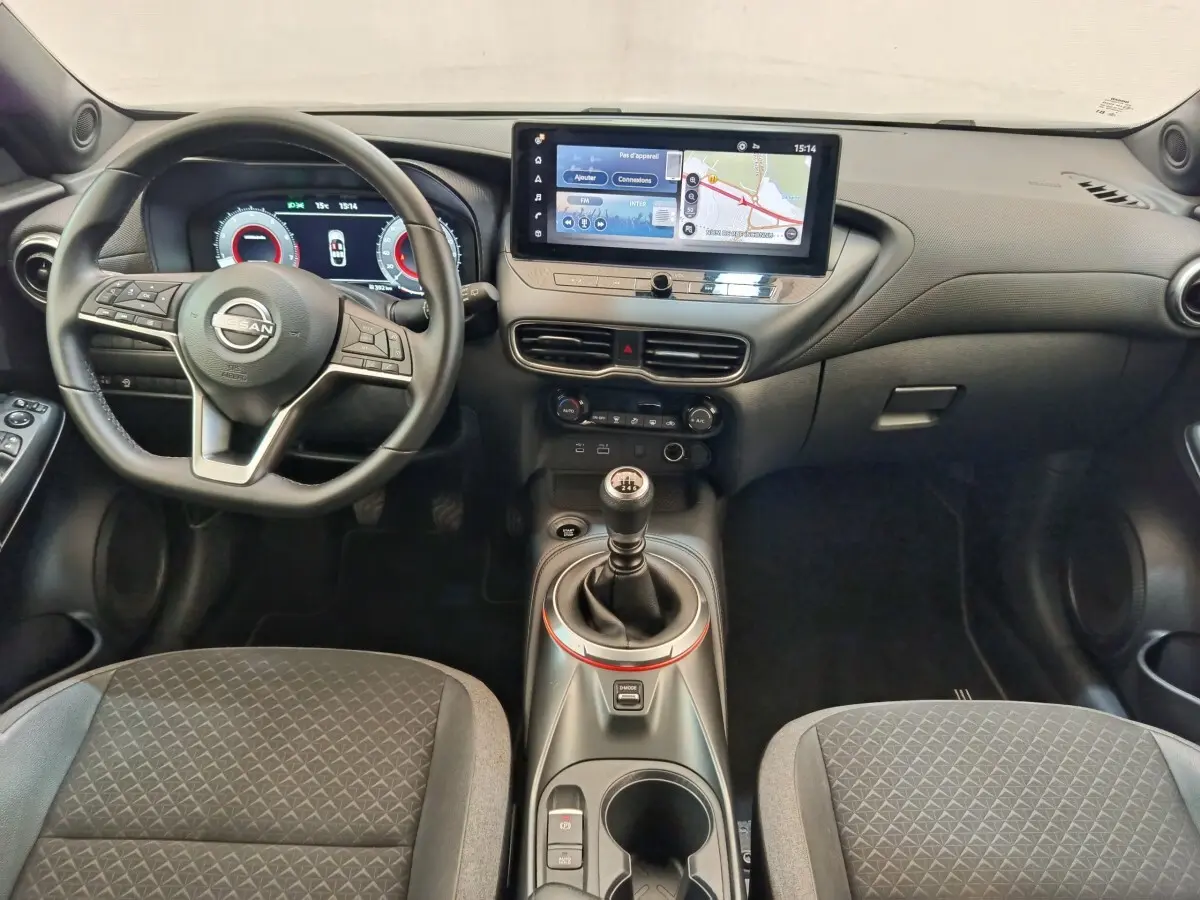 Vue intérieure avant du Nissan Juke 2025 gris clair, avec tableau de bord numérique et écran tactile central large.