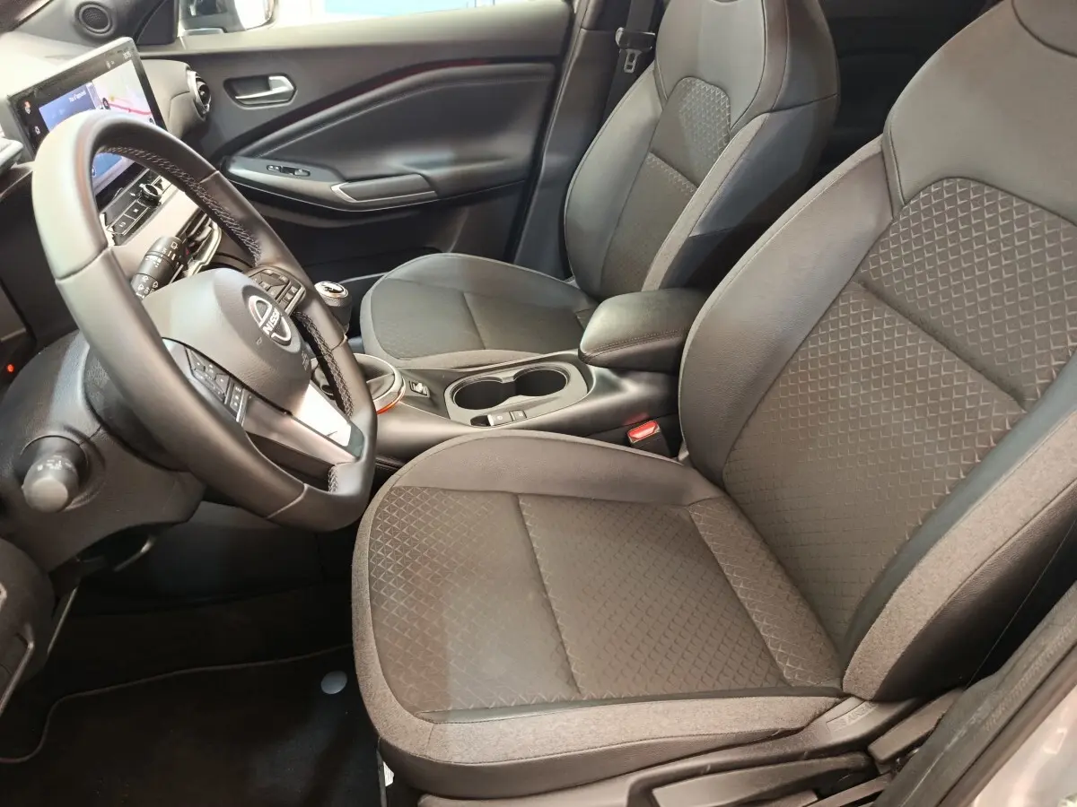 Vue intérieure côté conducteur du Nissan Juke gris clair 2025, avec sièges tissu et volant multifonctions.