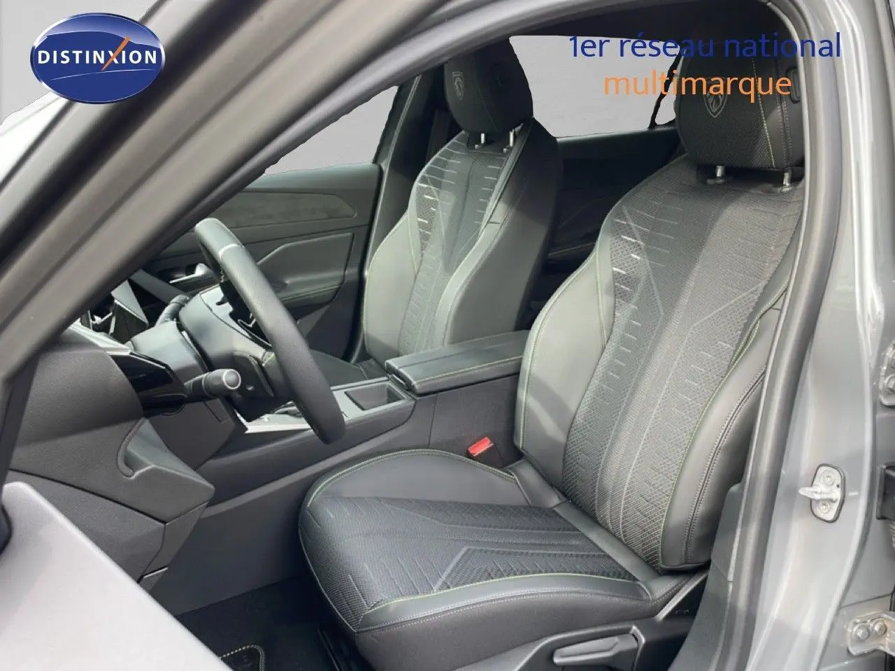Vue intérieure côté conducteur de la Peugeot 308 gris selenium, sièges tissu cuir avec surpiqûres vertes et volant multifonction.