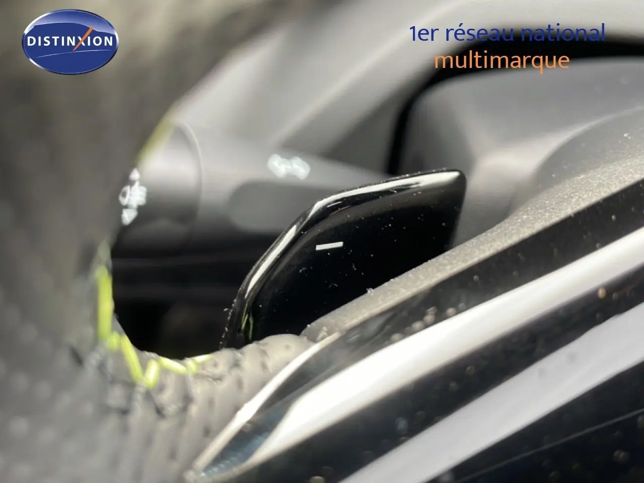 Gros plan sur la palette de changement de vitesse noire et brillante derrière le volant perforé d’une Peugeot 308 gris selenium.