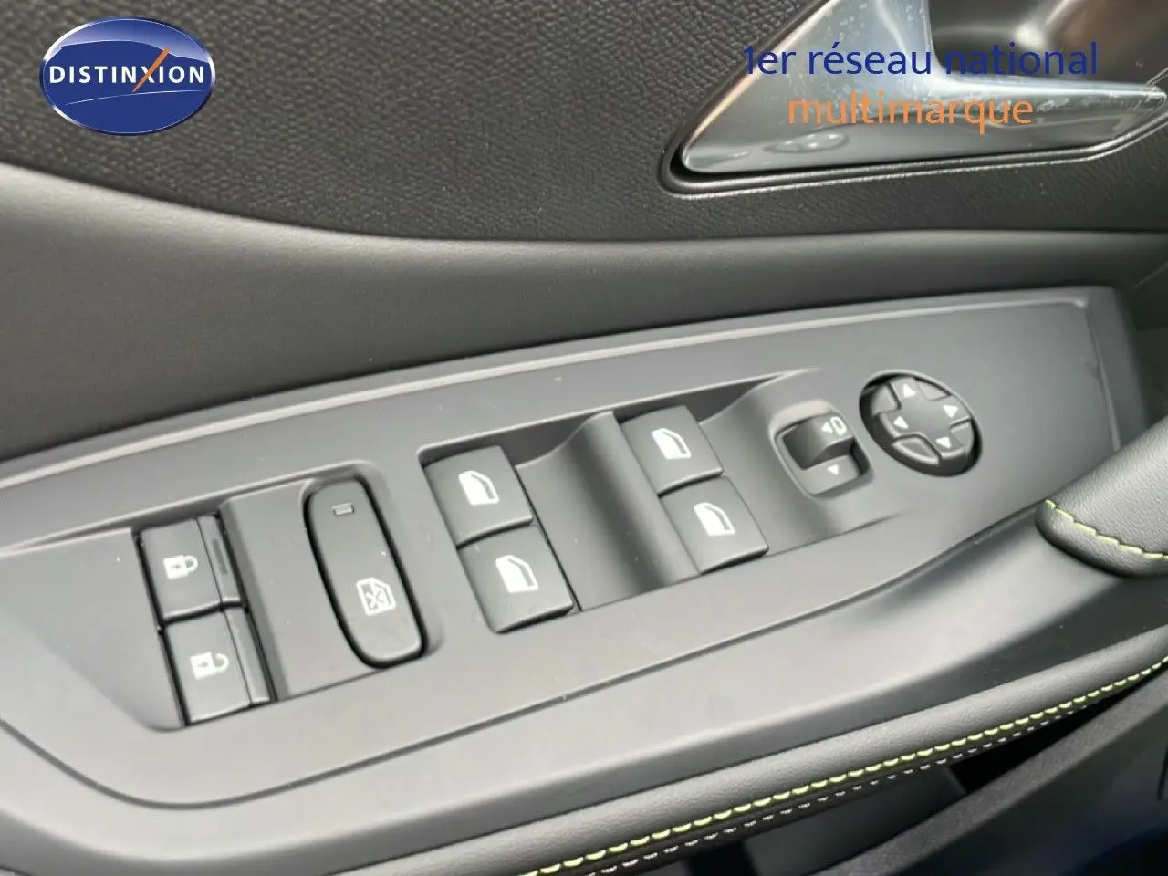 Gros plan sur la commande des vitres côté gauche d’une Peugeot 308 gris selenium, avec surpiqûres vertes visibles.