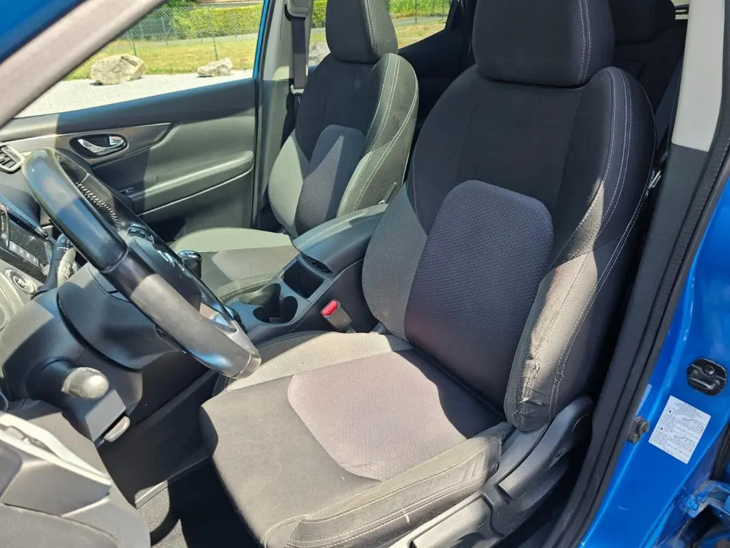 Vue intérieure côté conducteur du Nissan Qashqai bleu 2019, montrant les sièges en tissu noir et le volant.