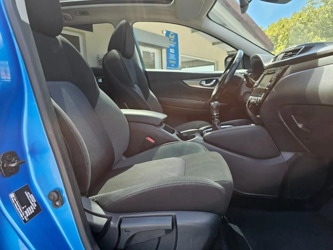 Intérieur du Nissan Qashqai bleu 2019, vue côté conducteur, sièges noirs et levier de vitesse manuel visible.