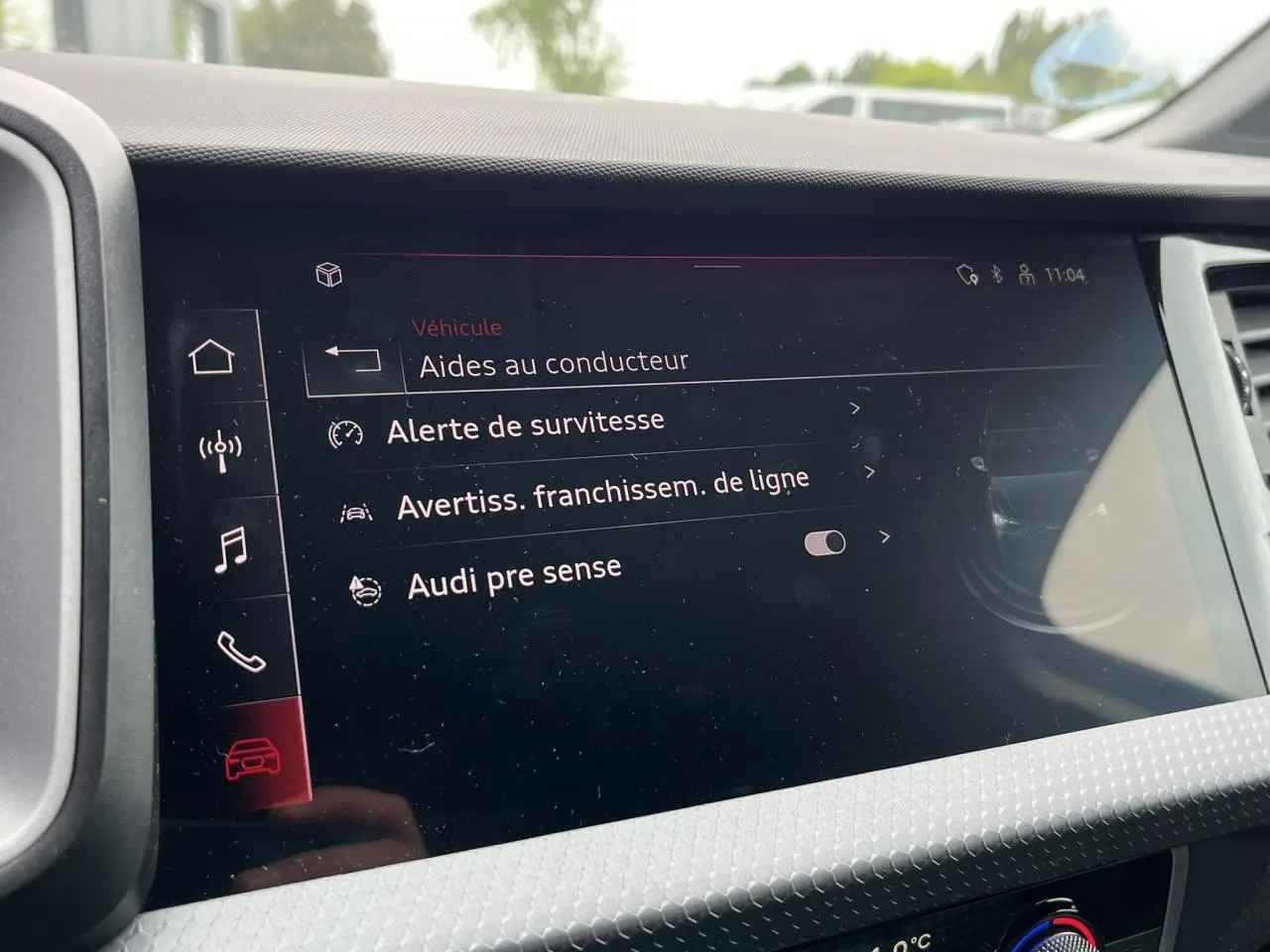 Écran tactile intérieur affichant les aides à la conduite de l'Audi A1 Sportback 25 TFSI rouge Misano, vue de face.