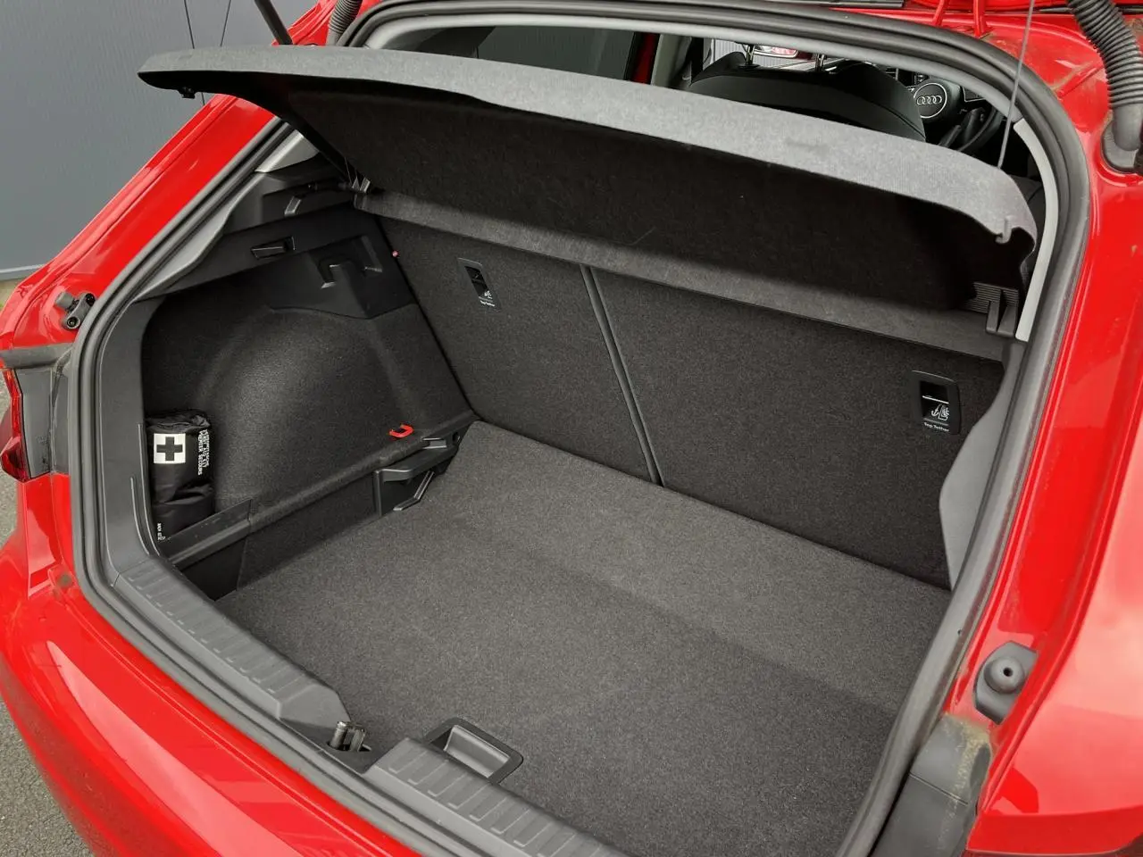 Coffre ouvert vu de l'arrière d'une Audi A1 Sportback rouge Misano avec intérieur de coffre gris et trousse de secours.