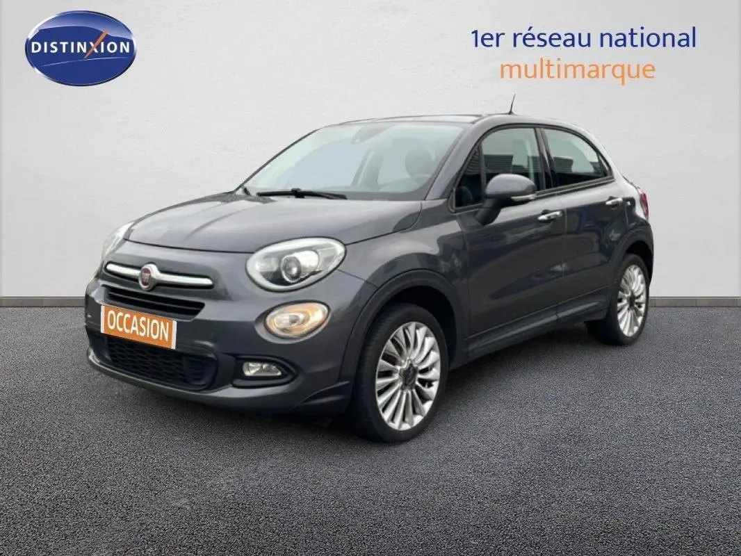 Fiat 500X gris foncé vue 3/4 avant droit, avec jantes alliage 18 pouces et phares antibrouillard allumés.