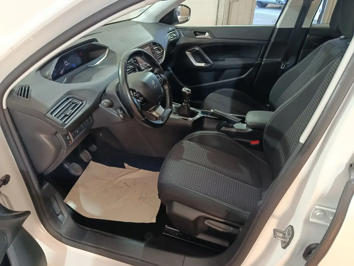 Intérieur côté conducteur d'une Peugeot 308 blanche 2021, volant cuir, sièges tissu noir et tableau de bord moderne.