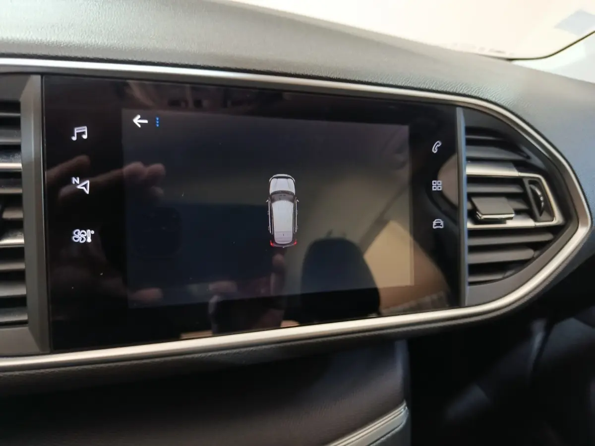 Écran tactile central affichant la vue aérienne du véhicule Peugeot 308 blanc, tableau de bord noir moderne.