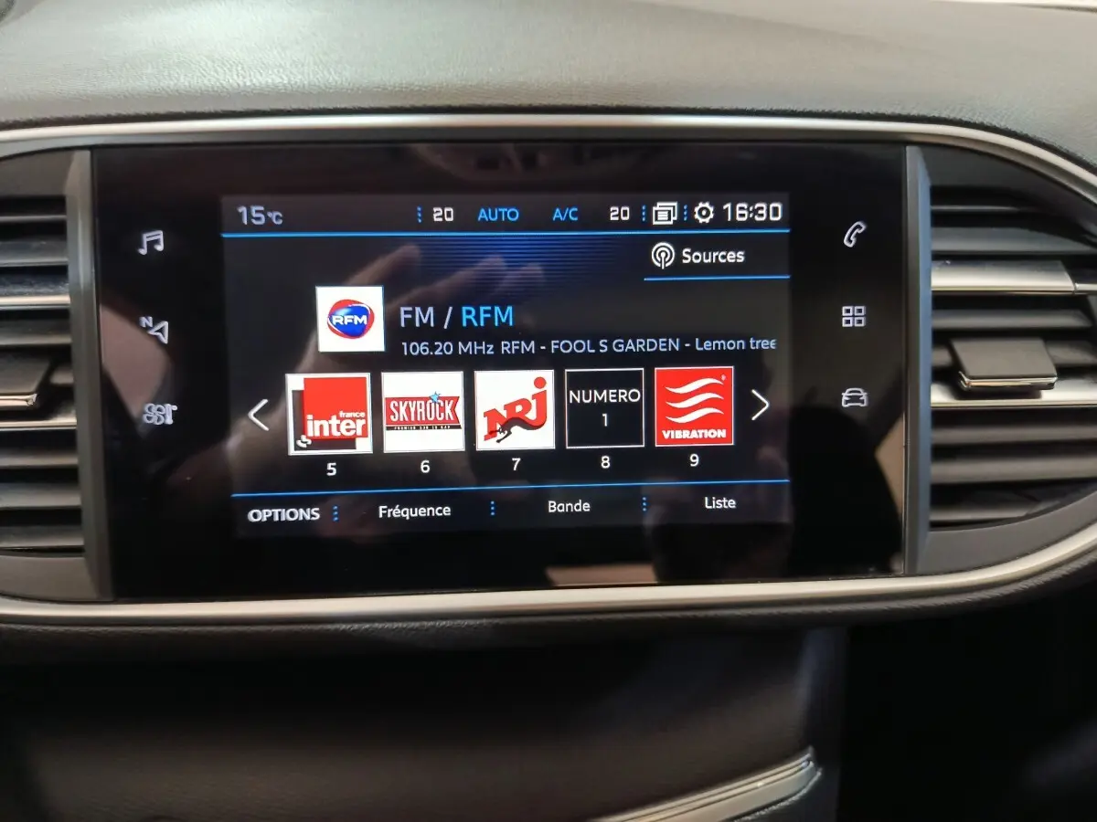 Écran tactile central de la Peugeot 308 blanc 2021 affichant les stations radio avec commandes autour en noir et beige.