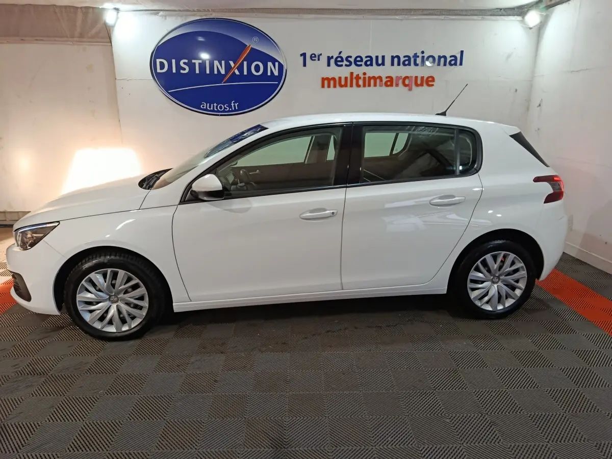 Profil côté gauche d'une Peugeot 308 blanche 2021, finition Premium Pack, dans un showroom avec logo Distinxion en arrière-plan.