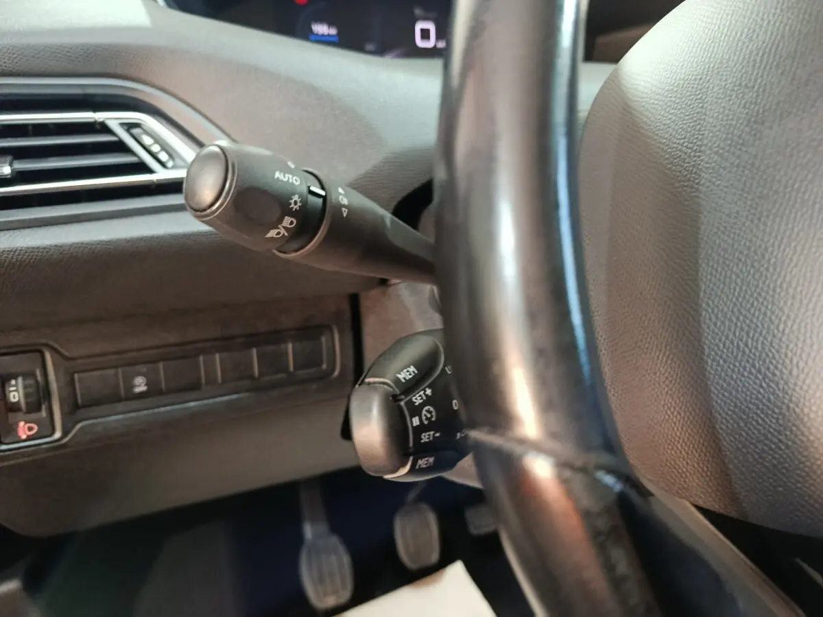 Gros plan sur la colonne de direction et commandes au volant cuir noir d'une Peugeot 308 blanche de 2021.